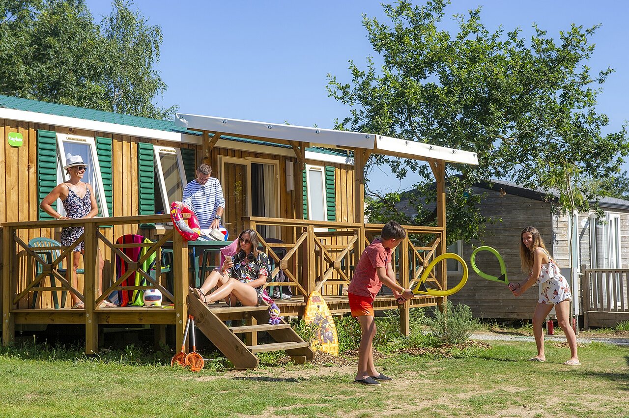 Family playing in front of a mobile home with terrace at CAPFUN Heino campsite in Heino.