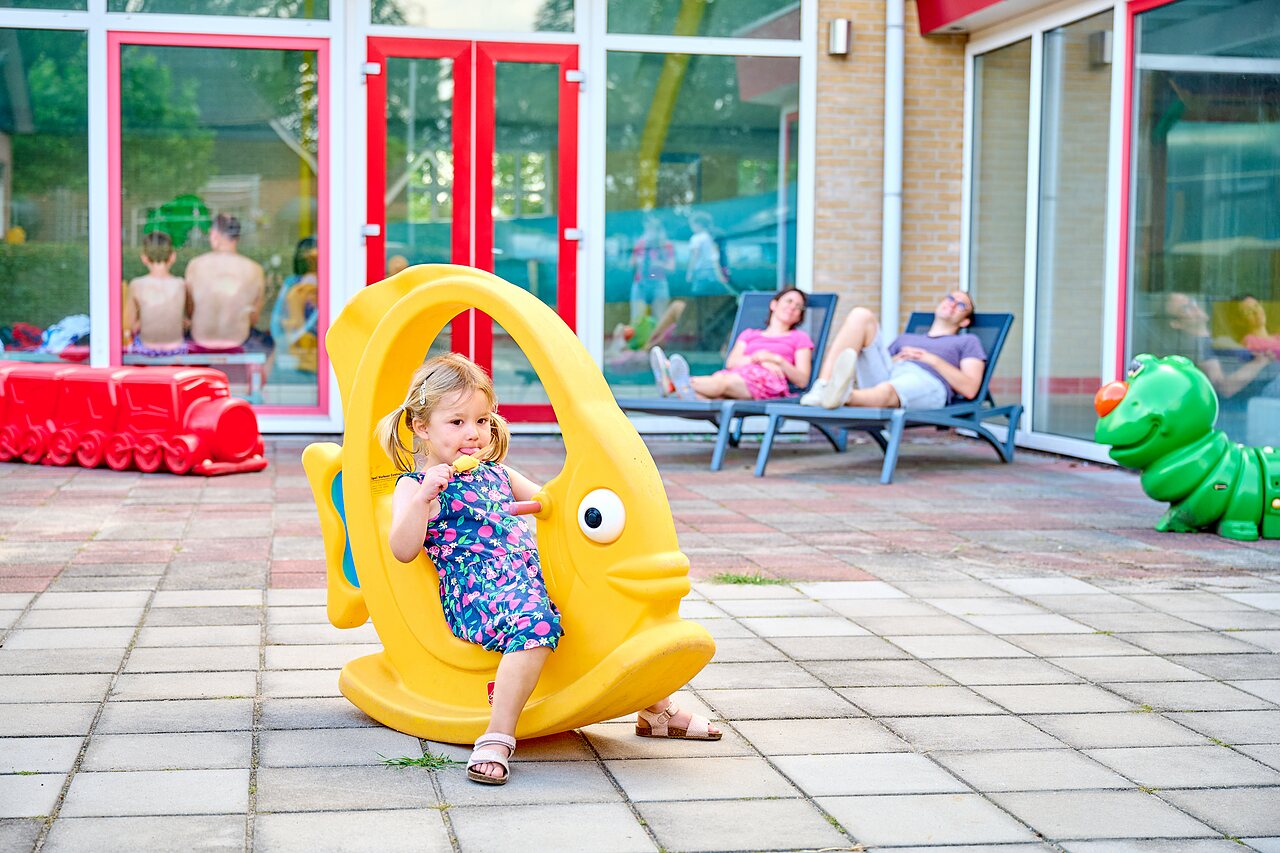 Girl on fish spring rider, playground near pool at CAPFUN Heino, Heino.
