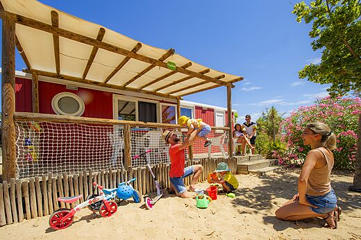Red Mobile home with terrace, family and children playing at CAPFUN Hermitage campsite in SERIGNAN (34).