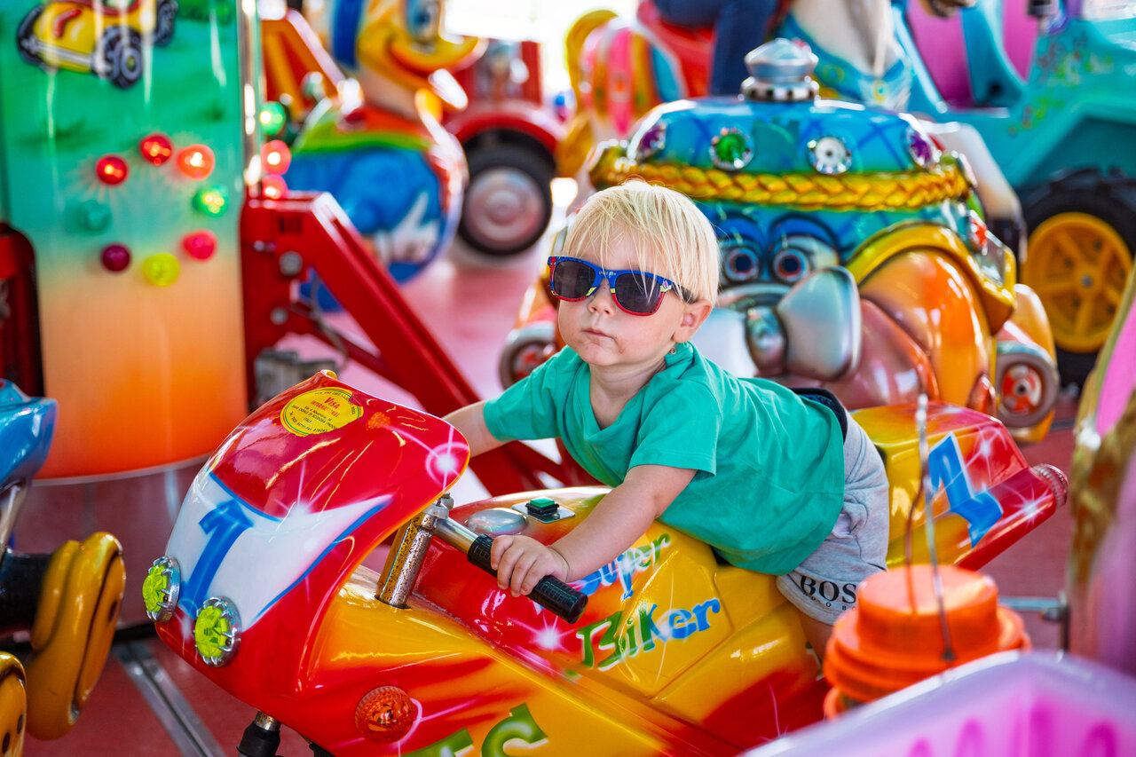 Young blonde child on coin-operated motorcycle ride, at CAPFUN Hirondelle campsite in Oteppe.