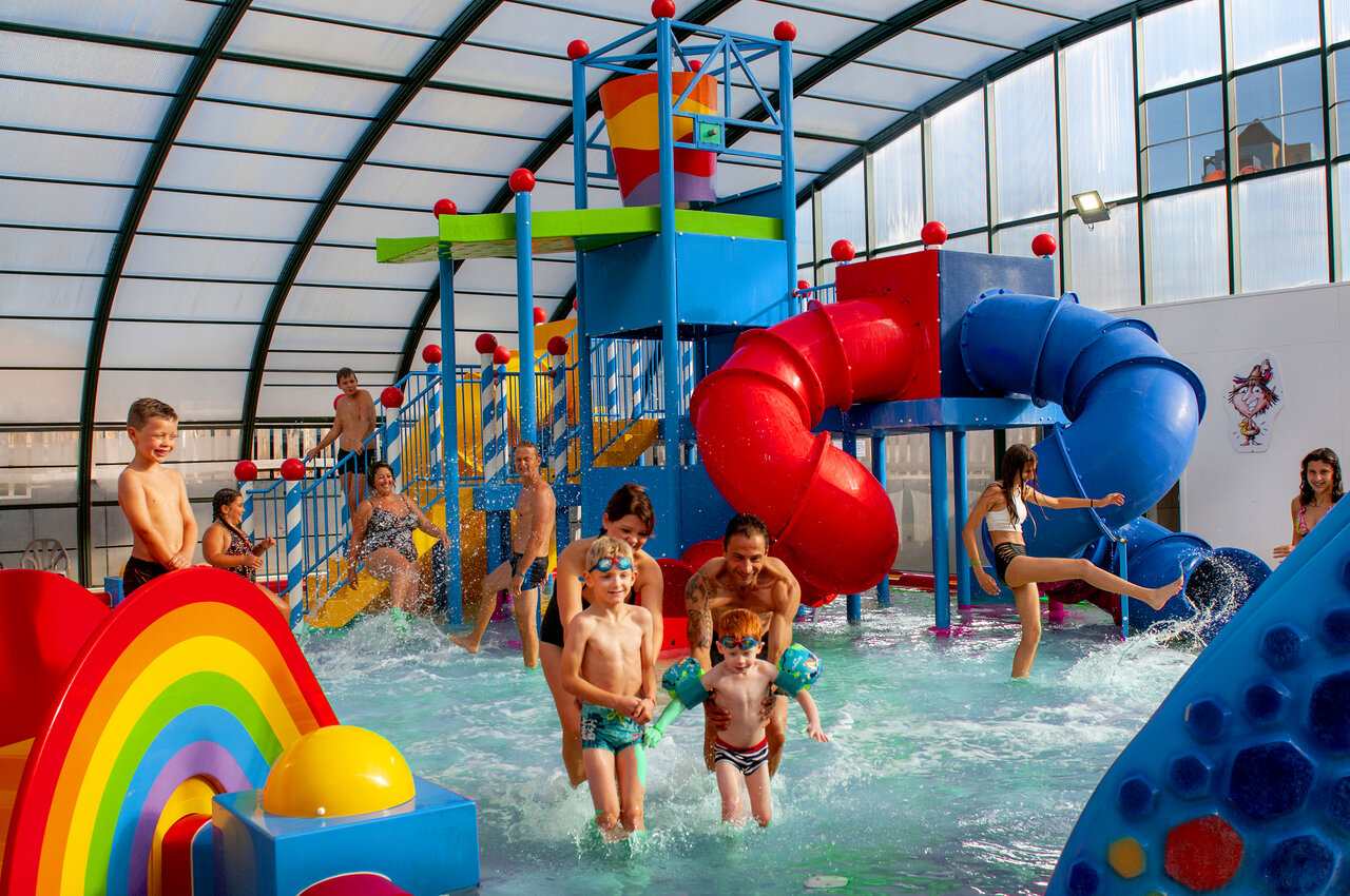Covered water park with colorful slides and water games at CAPFUN Hirondelle campsite in Oteppe.