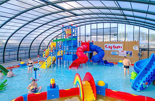 Indoor swimming pool with water slides and water games at CAPFUN Hirondelle campsite in Oteppe.