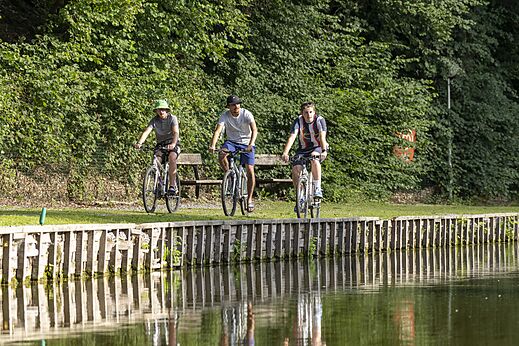 Three people cycling along a waterway at CAPFUN Hirondelle campsite in Oteppe.