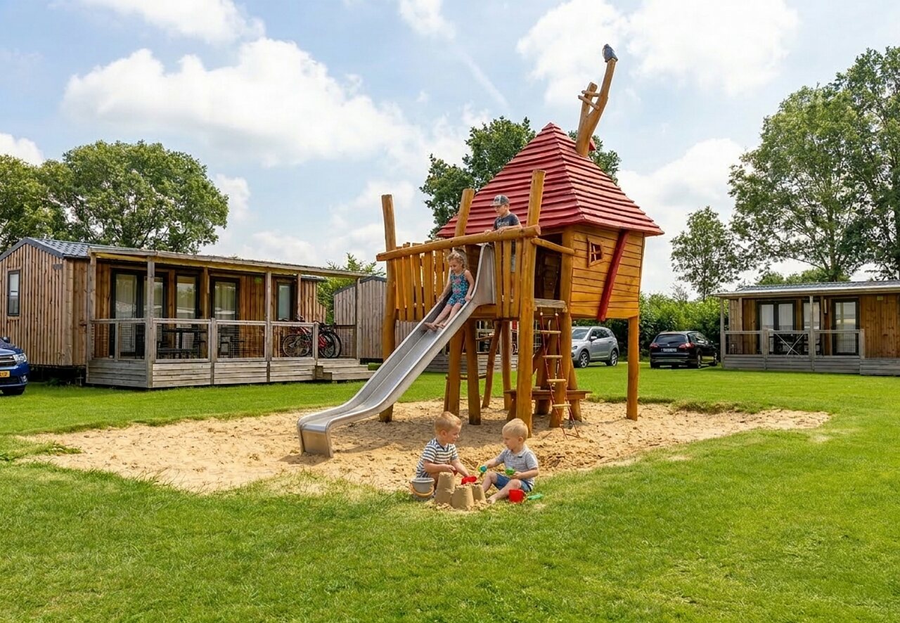 Wooden playground with slide and children, mobile homes at CAPFUN IJsselstrand campsite in Doesburg.