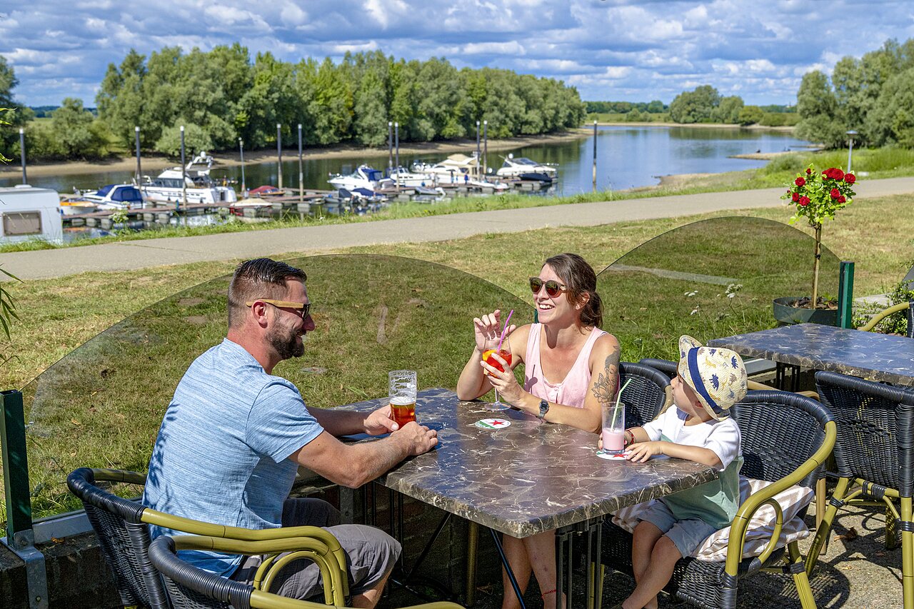 Smiling family enjoying drinks on terrace by marina at CAPFUN IJsselstrand campsite in Doesburg.