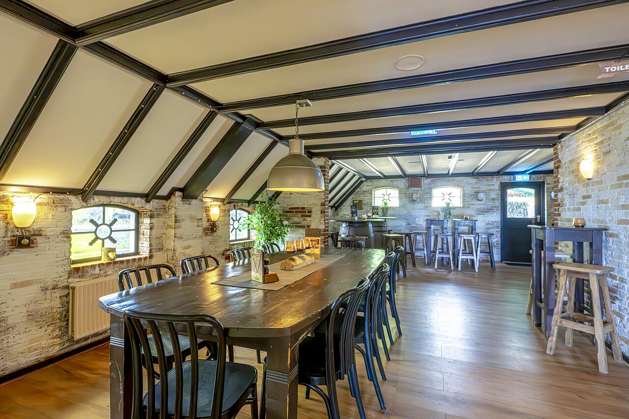 Restaurant dining room with long table and bar at CAPFUN IJsselstrand campsite in Doesburg.