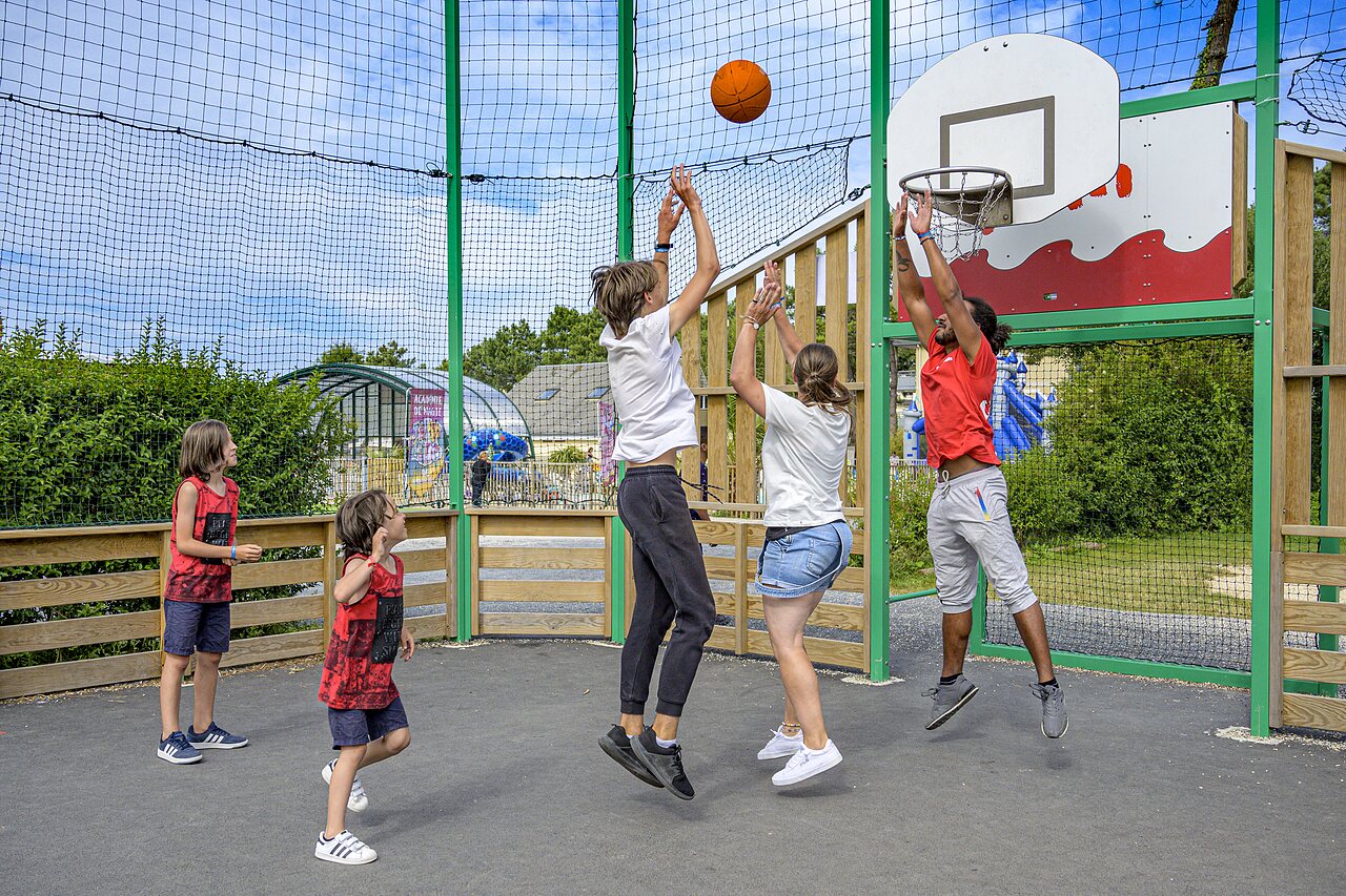 Family and animator play basketball on multisport court at CAPFUN Joncal.
