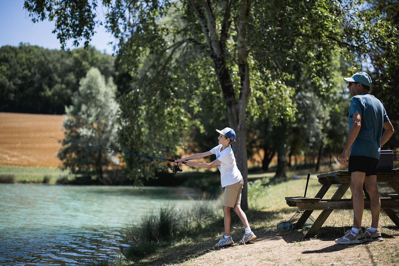 Child fishing at the lake with an adult at CAPFUN Lac des 3 Vall�es campsite.