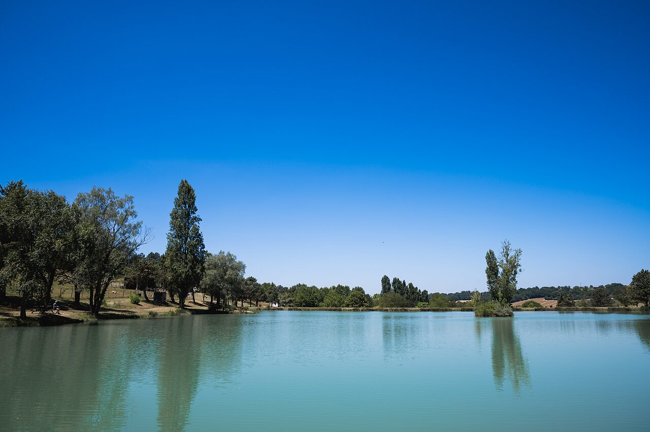 Large natural lake surrounded by trees at CAPFUN Lac des 3 Vall�es campsite in Lectoure.