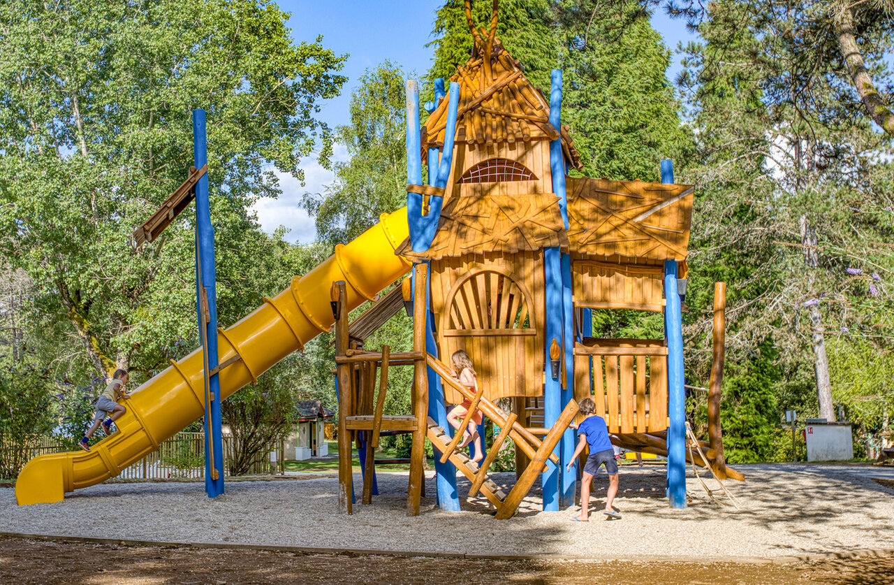Wooden playground with yellow slide at CLICOCHIC Lac de Miel campsite in Beynat (19).