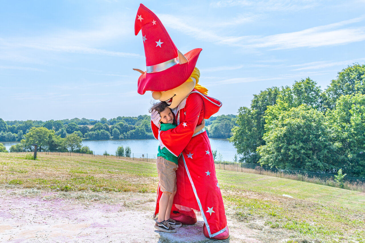 Child hugging camping mascot, lake in background at CAPFUN Lac de Ribou.