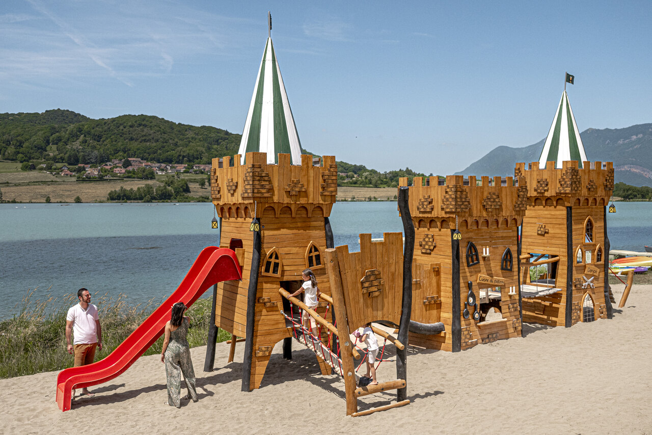 Large wooden castle playground with slide by the lake at camping CLICOCHIC Lac du Lit du Roi in Massignieu-de-Rives (01).