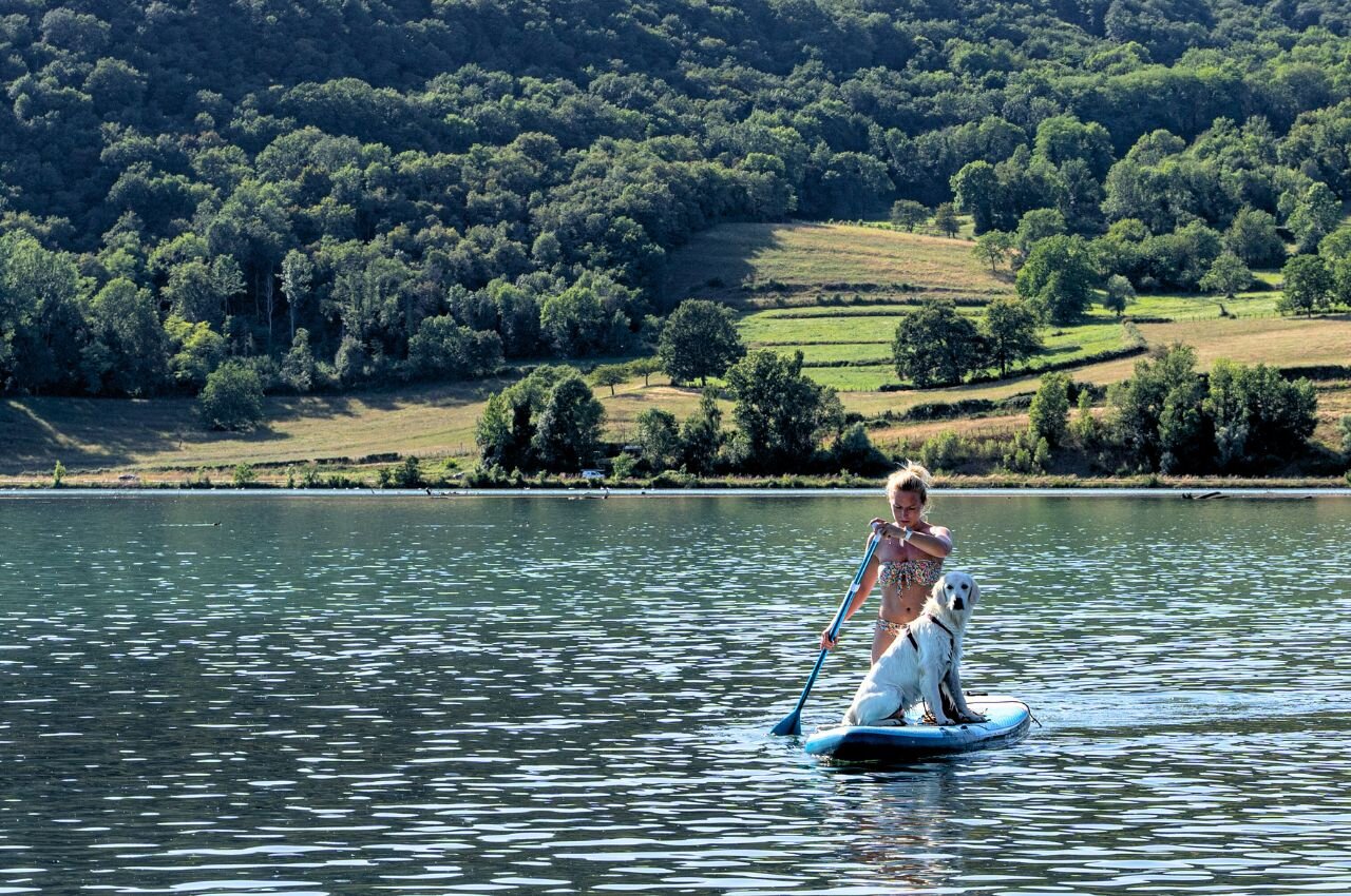 Woman and dog on paddleboard, lake. At camping CLICOCHIC Lac du Lit du Roi.