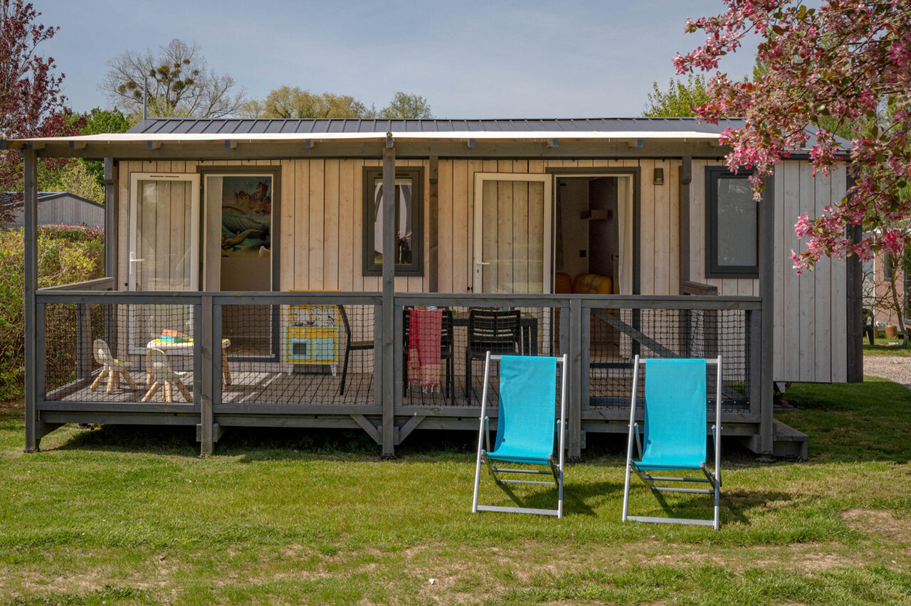 Modern mobile home with covered terrace and deck chairs at CLICOCHIC Lac du Lit du Roi campsite in Massignieu-de-Rives (01).