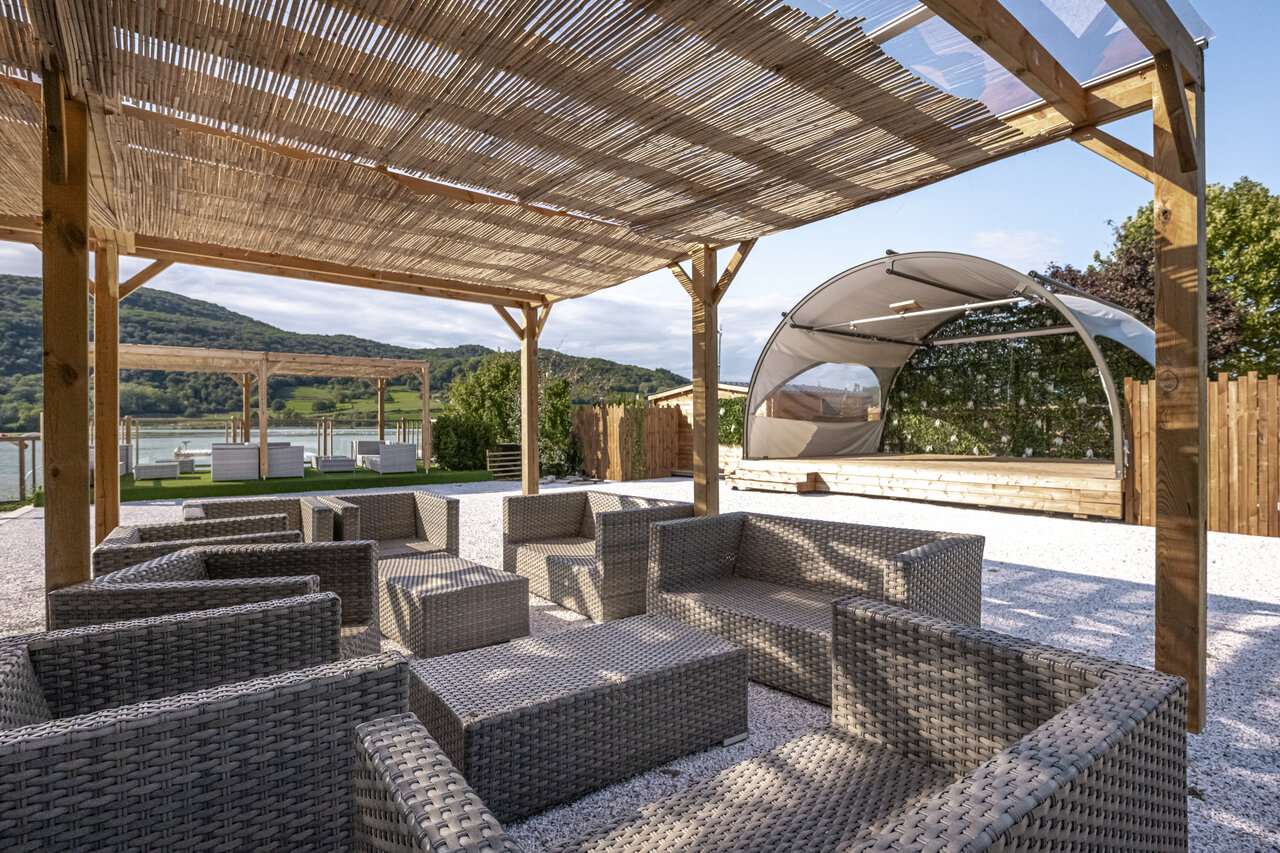 Outdoor lounge, stage, lake view at CLICOCHIC Lac du Lit du Roi campsite in Massignieu-de-Rives (01).