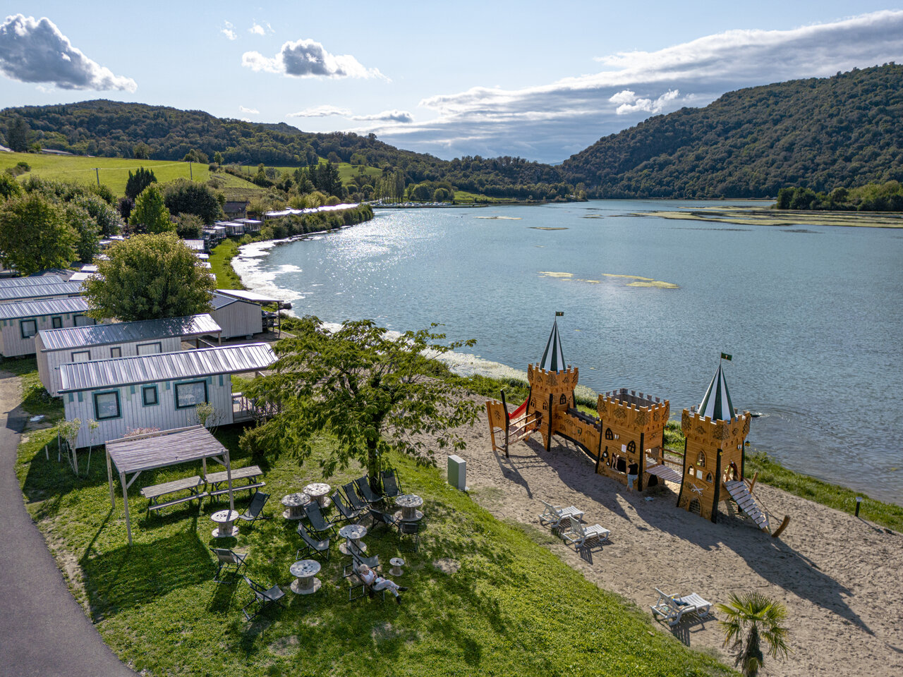 Aerial view of lake, mobile homes and playground at CLICOCHIC Lac du Lit du Roi campsite in Massignieu-de-Rives (01).