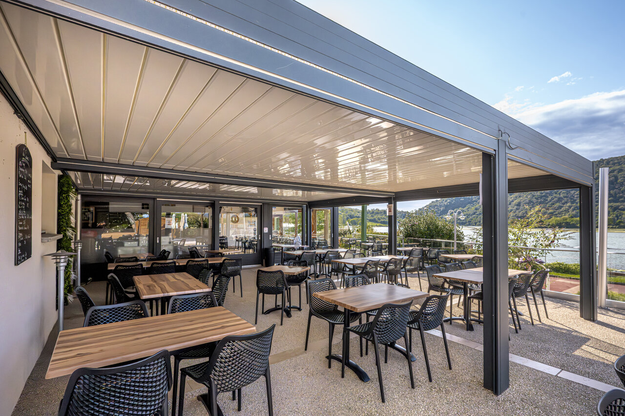 Modern restaurant-bar terrace with lake view at CLICOCHIC Lac du Lit du Roi campsite in Massignieu-de-Rives (01).