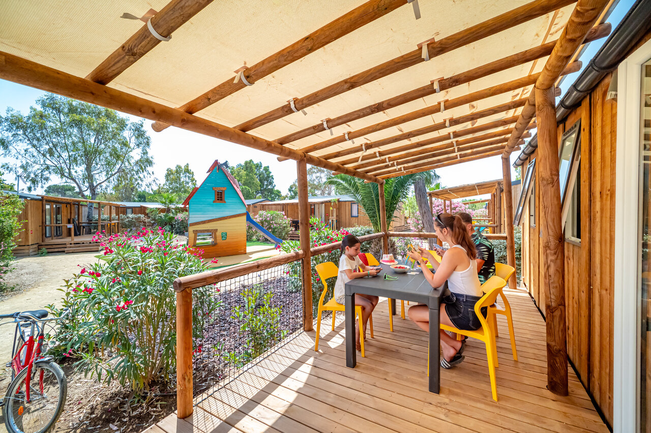Family dining on mobile home terrace with playground at CAPFUN Las Bousigues campsite in Le Barcar�s.