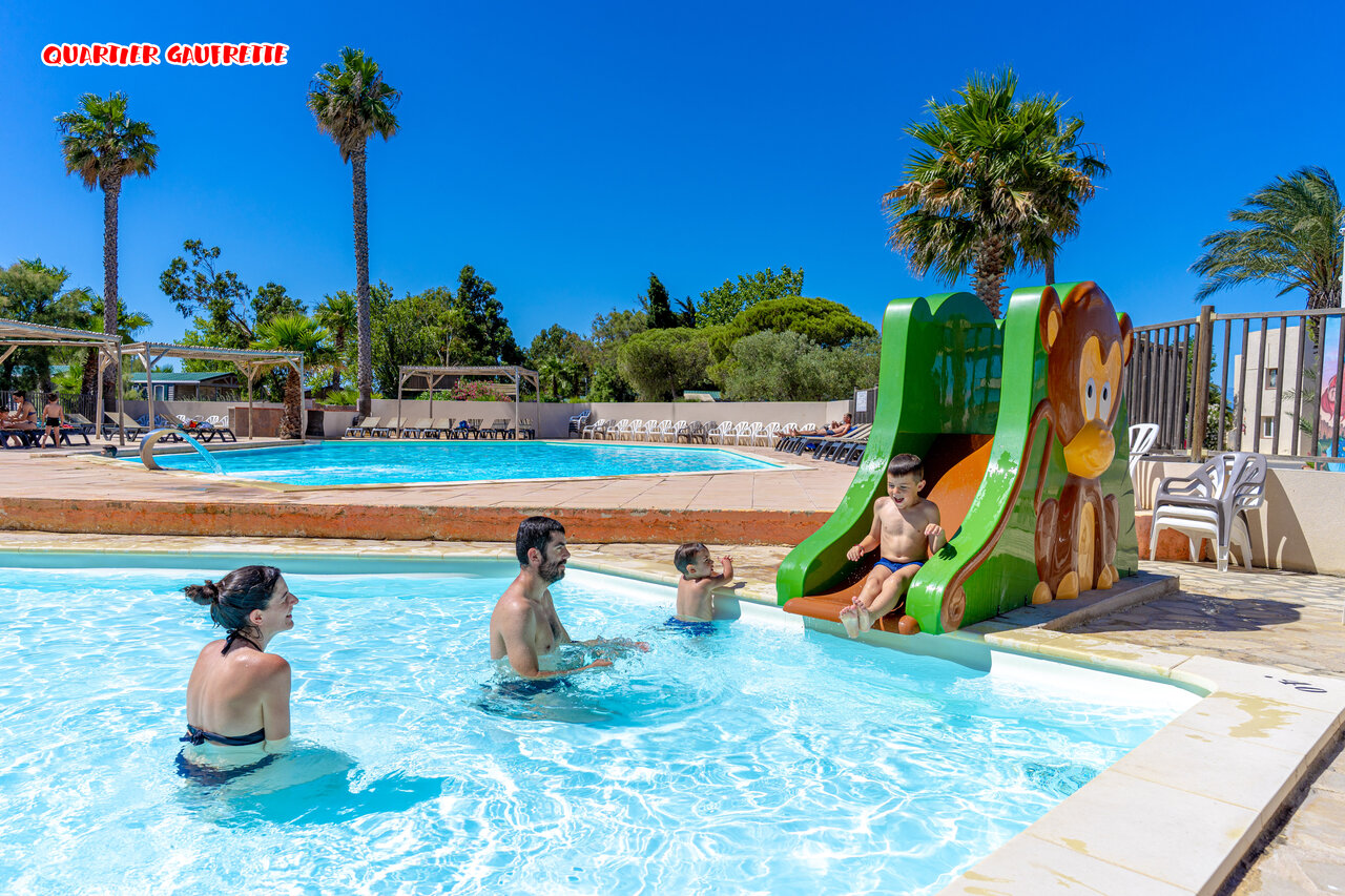 Family swimming pool with children's slide and palm trees at CAPFUN Las Bousigues campsite in Le Barcar�s (66).