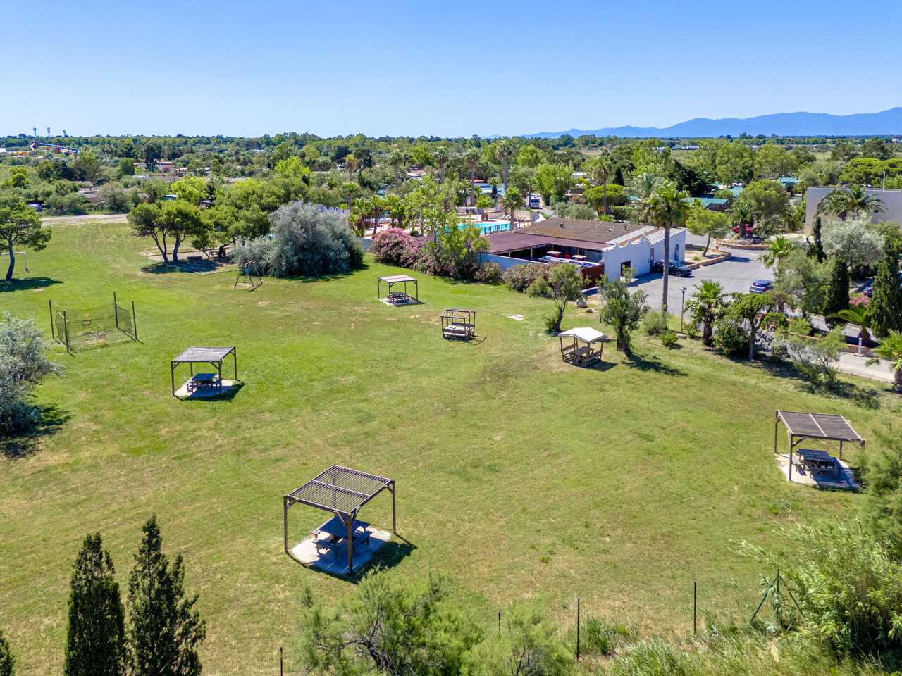 Grassy area, picnic tables, swimming pool at CAPFUN Las Bousigues campsite.