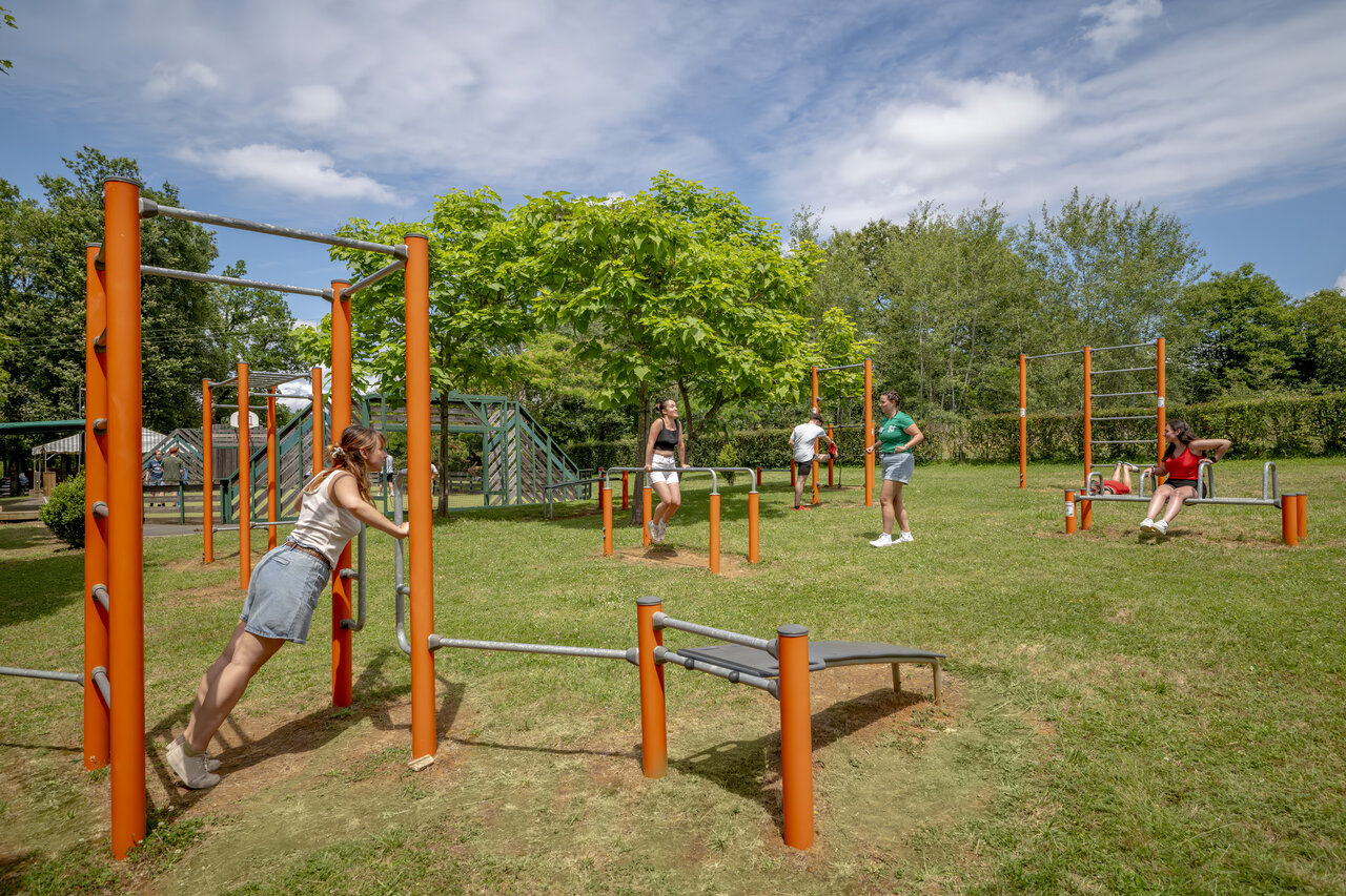 Adults training on outdoor fitness equipment at CLICOCHIC Linotte campsite in Le Bugue.