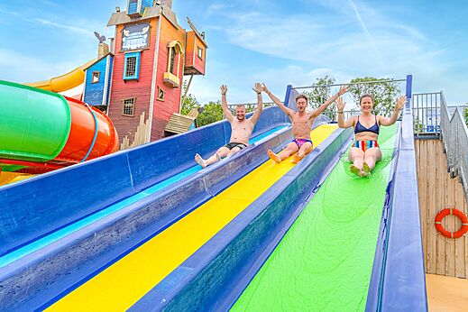 Three people sliding down colorful water slides at CAPFUN Lodge campsite in SARZEAU (56).