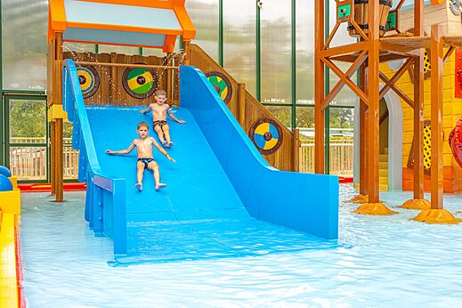 Two children on blue water slide in indoor pool at CAPFUN Lodge campsite in SARZEAU (56).