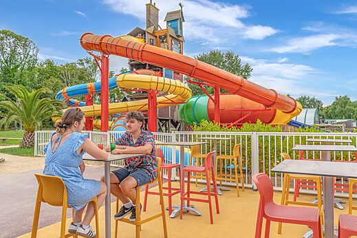 Colorful water slides and outdoor bar terrace at CAPFUN Lodge campsite in SARZEAU (56).