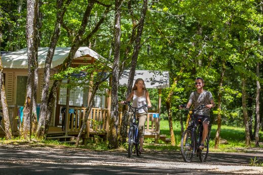 Couple cycling on wooded path near Mobil-homes at CLICOCHIC Lou Castel campsite.