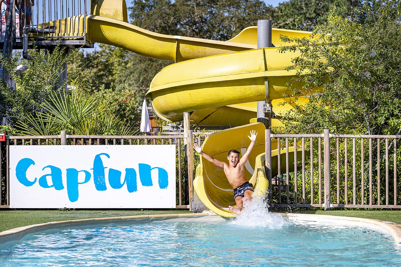 Yellow water slide and child in the swimming pool at CAPFUN Lou Puntaou campsite in LEON.