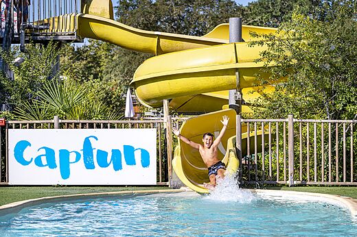 Yellow water slide and child in the swimming pool at CAPFUN Lou Puntaou campsite in LEON.