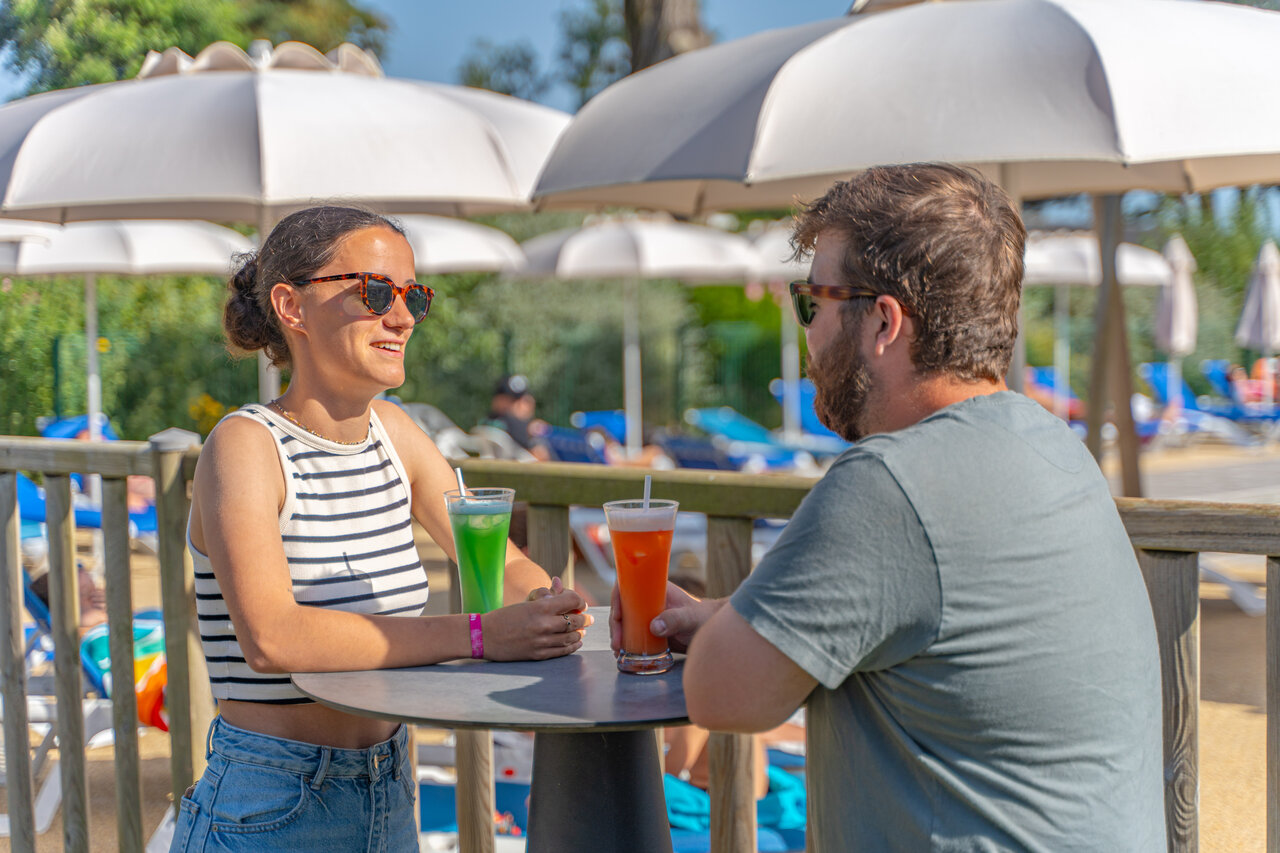 Smiling couple enjoying drinks at the pool bar at CAPFUN Madrague campsite in PORNIC (44).