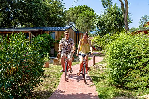 Smiling couple cycling on path at CAPFUN Mael campsite in ARGELES.