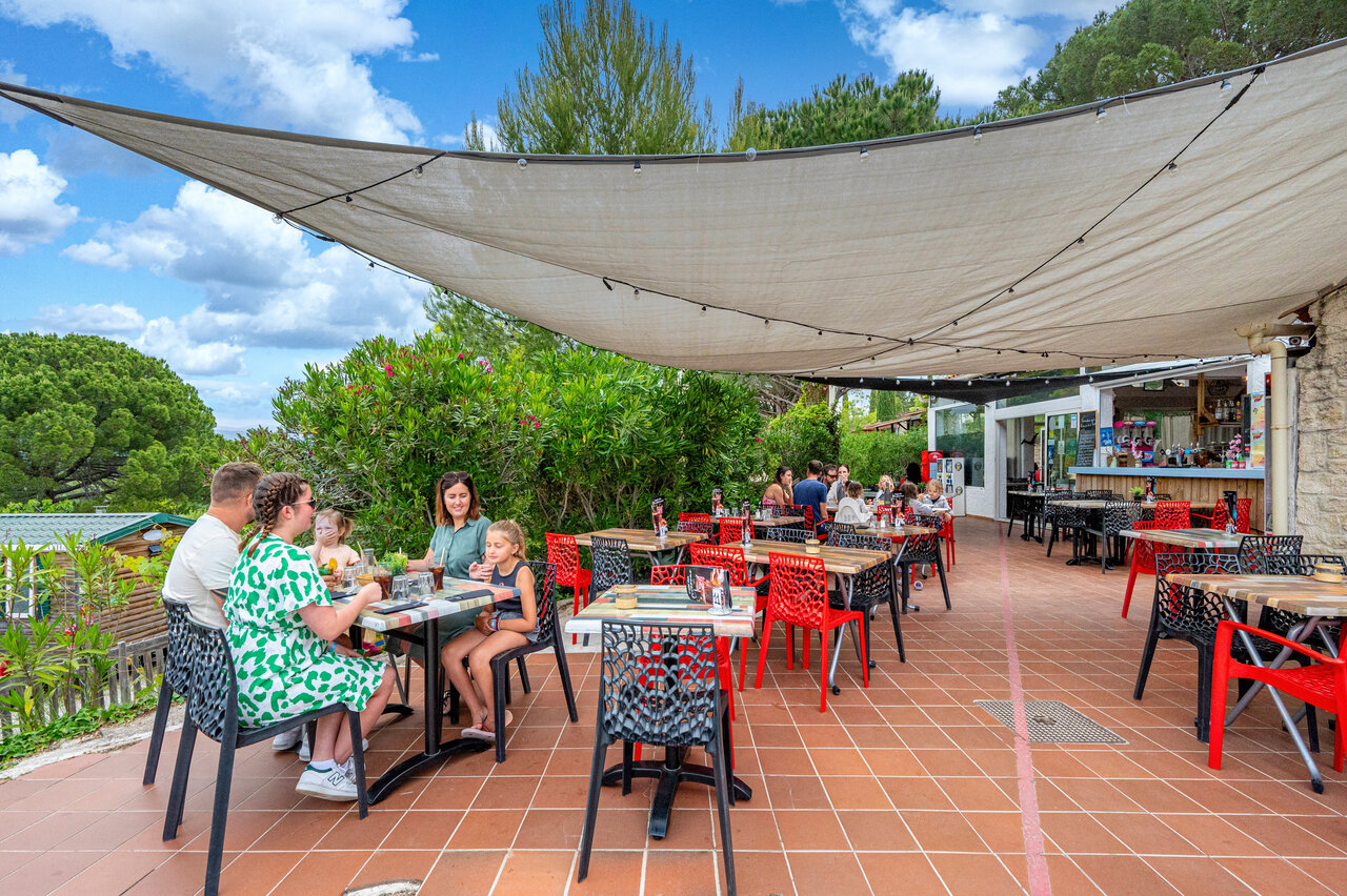 Shaded restaurant terrace with families and bar at CAPFUN Malissonne campsite in LA CADIERE D'AZUR (83)