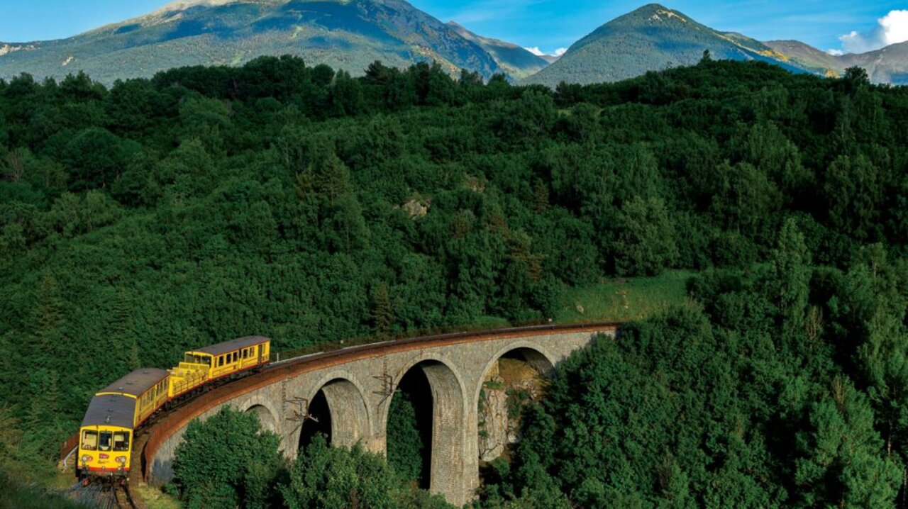 Yellow train on viaduct, mountains, at VAGUES OCEANES Marinette campsite in Ste Marie La Mer (66).