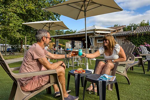 Couple toasting with cocktails at the bar of camping CLICOCHIC Médoc Bleu in Carcans (33).