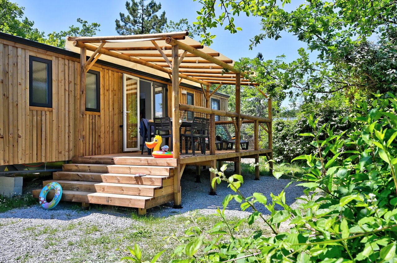 Wooden Mobile home with shaded terrace, outdoor furniture and greenery at CAPFUN Merle Roux campsite in Baix (07).