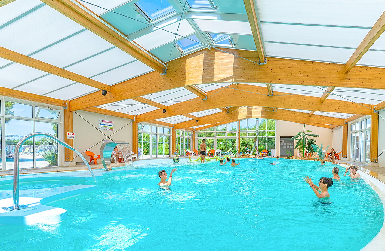 Indoor swimming pool with water features and swimmers at VAGUES OCEANES Micheli�re campsite in Givrand (85).