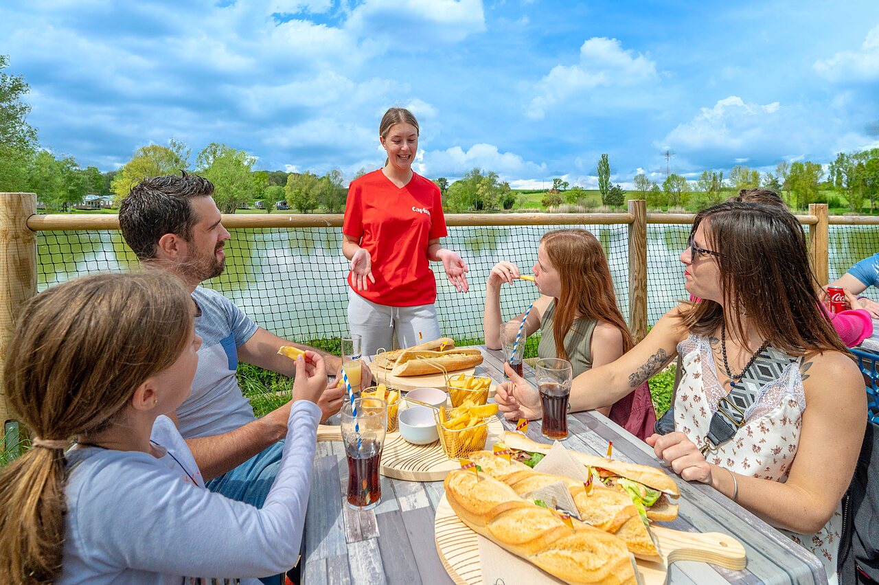 Family dining on terrace with lake view, at CAPFUN Mirabelle campsite in VOLSTROFF (57).