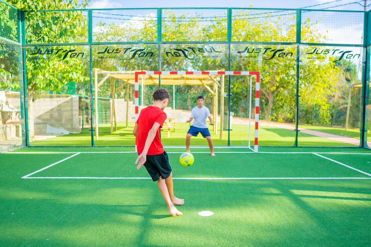 Young people playing football on multisport pitch at CAPFUN Mirmanda campsite.