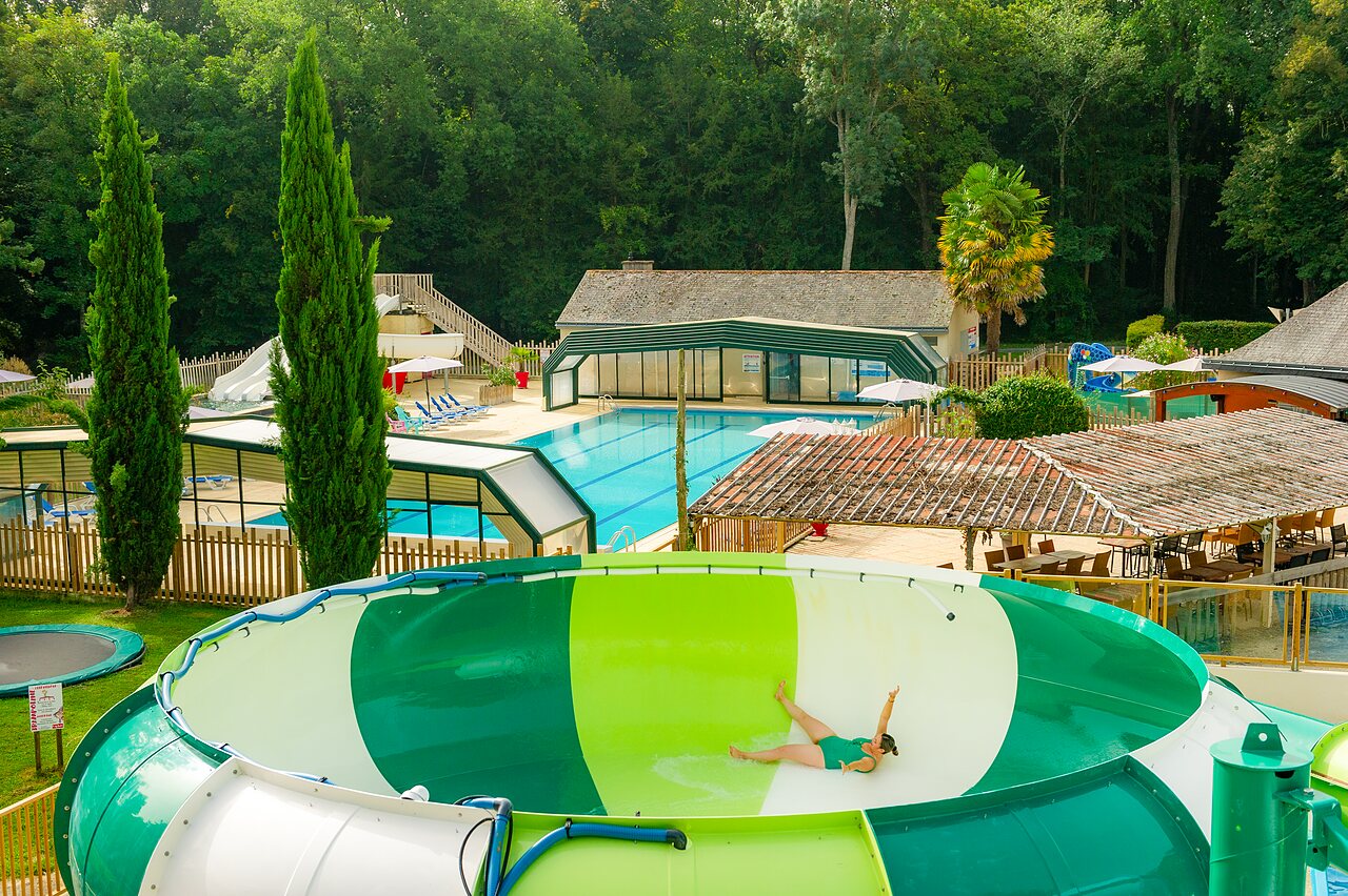 Woman on giant water slide, pools and greenery at CAPFUN Montsabert campsite in COUTURES (49).