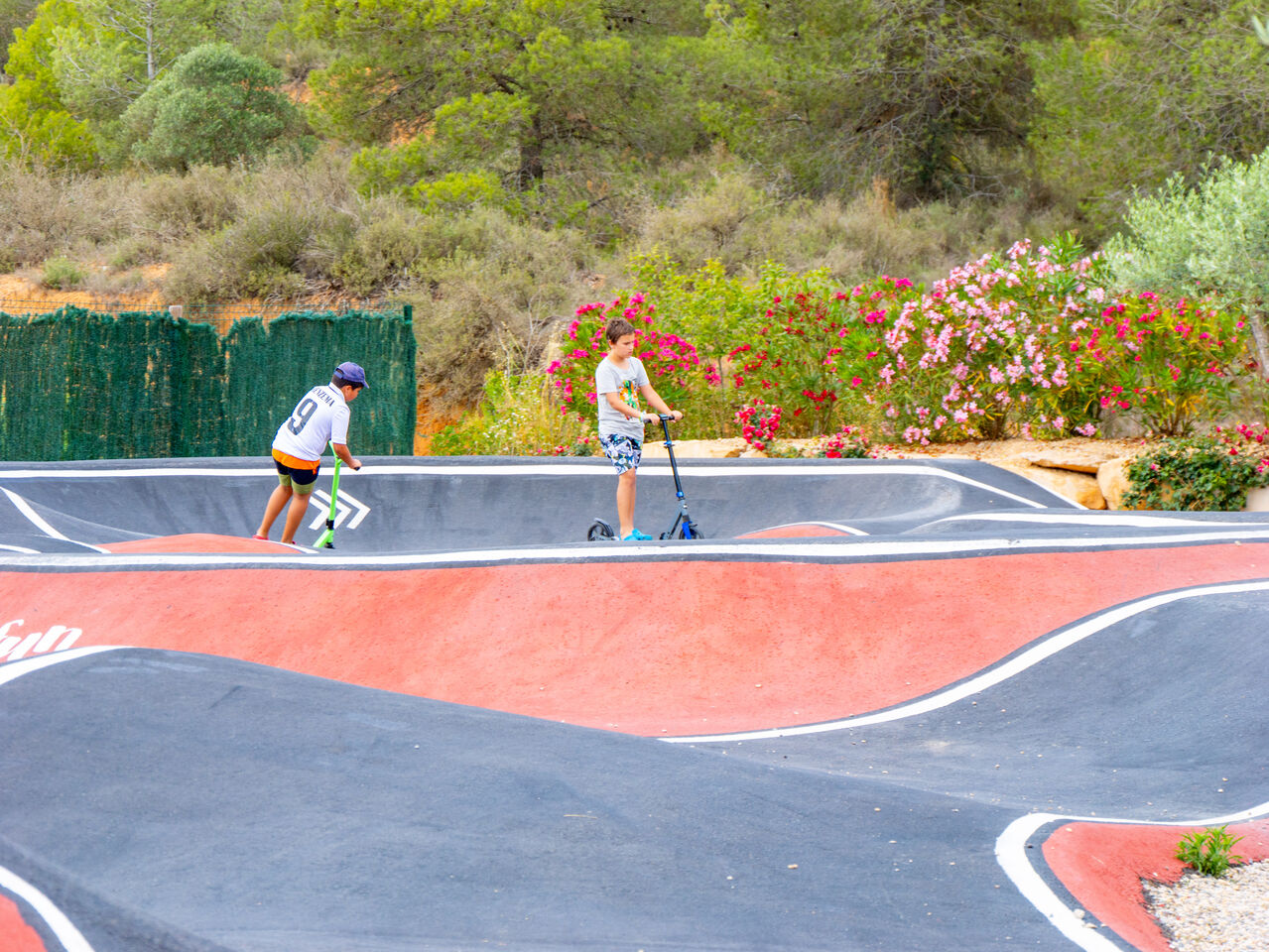 Pump track with children on scooters at CAPFUN Montblanc Park campsite in Montblanc (43).