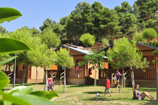 Wooden mobile homes with terraces, surrounded by trees at CAPFUN Montblanc Park campsite.