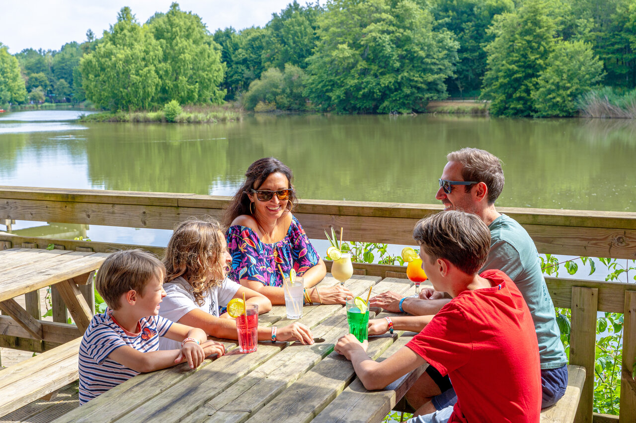 Smiling family enjoys cocktails at bar with lake view at CAPFUN Moulinal campsite in BIRON (24).