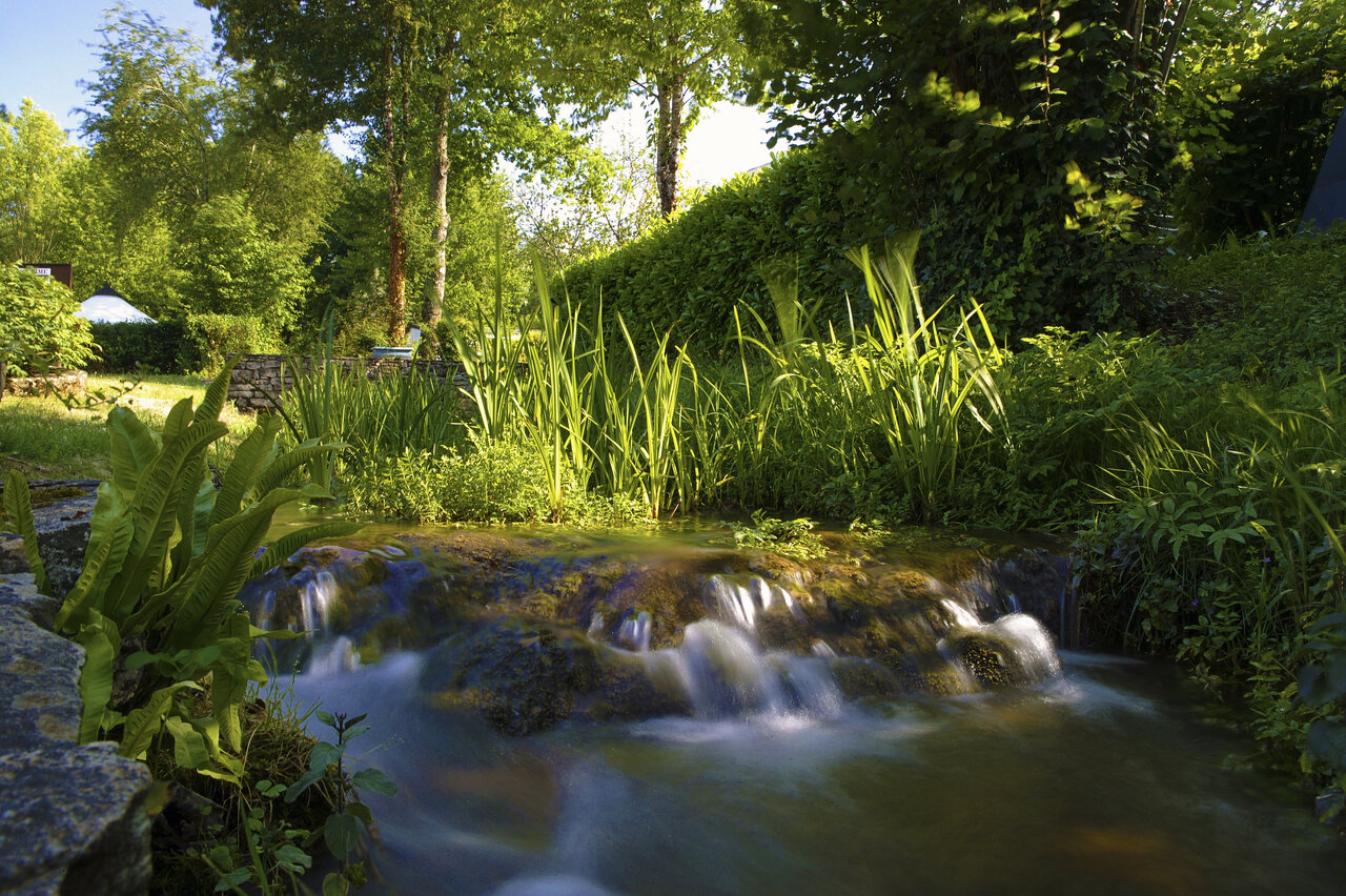 Natural waterfall and lush greenery at CLICOCHIC Moulin du Roch campsite in Saint Andre D'Allas.