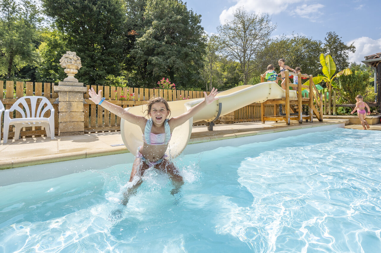 Girl on water slide, splashes in the pool at CLICOCHIC Moulin du Roch campsite.