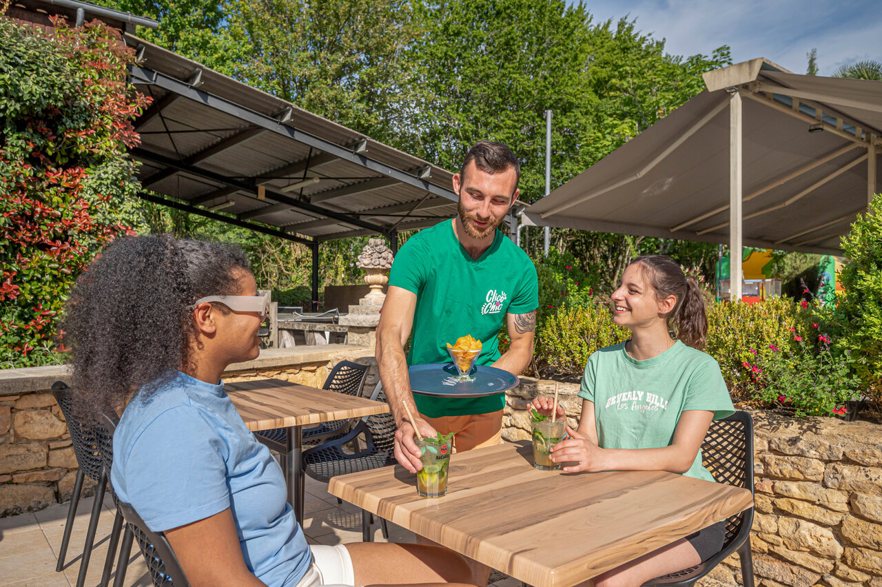 Waiter serving drinks on the terrace at camping CLICOCHIC Moulin du Roch in Saint Andre D'Allas (24).