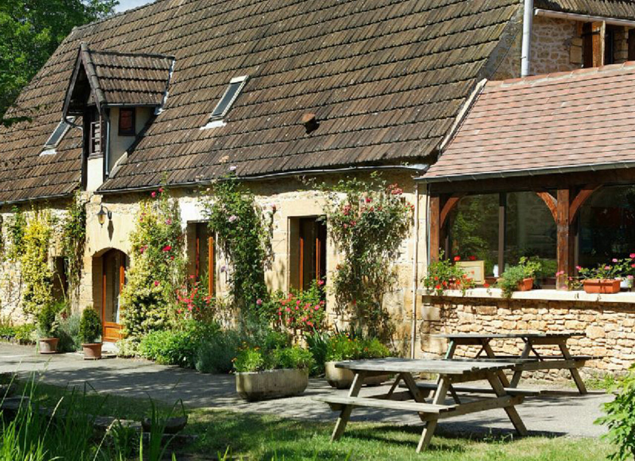 Stone building, picnic tables at CLICOCHIC Moulin du Roch campsite in Saint Andre D'Allas.