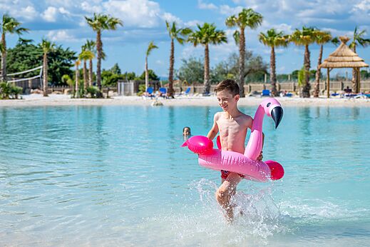 Swimming pool, child with flamingo float at CAPFUN La Nautique campsite in Narbonne.