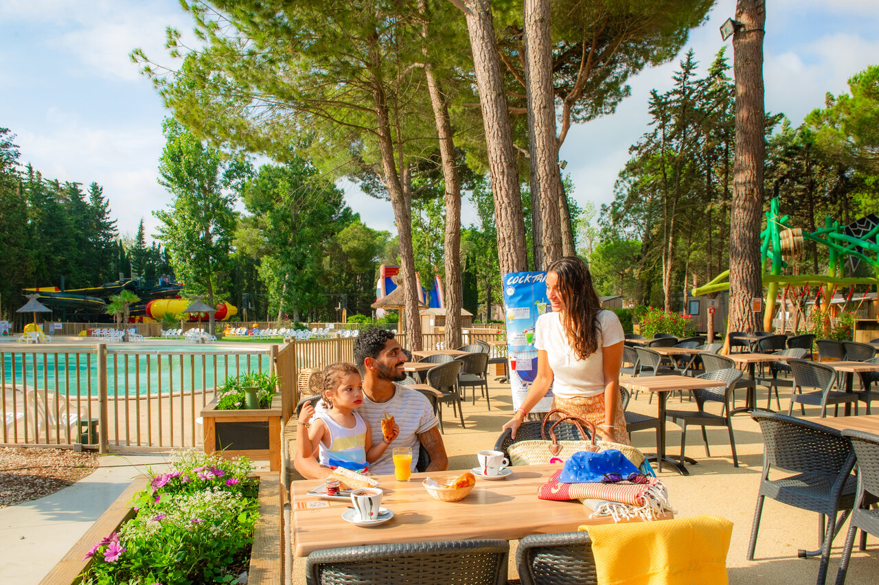 Family having breakfast on terrace near the pool at CAPFUN Or campsite in La Grande Motte (34).